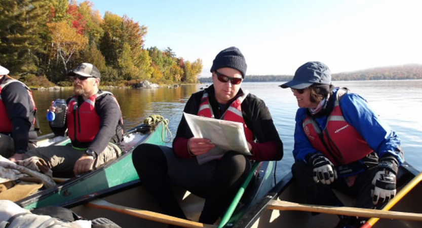 People sit in canoes floating close together and examine a map.